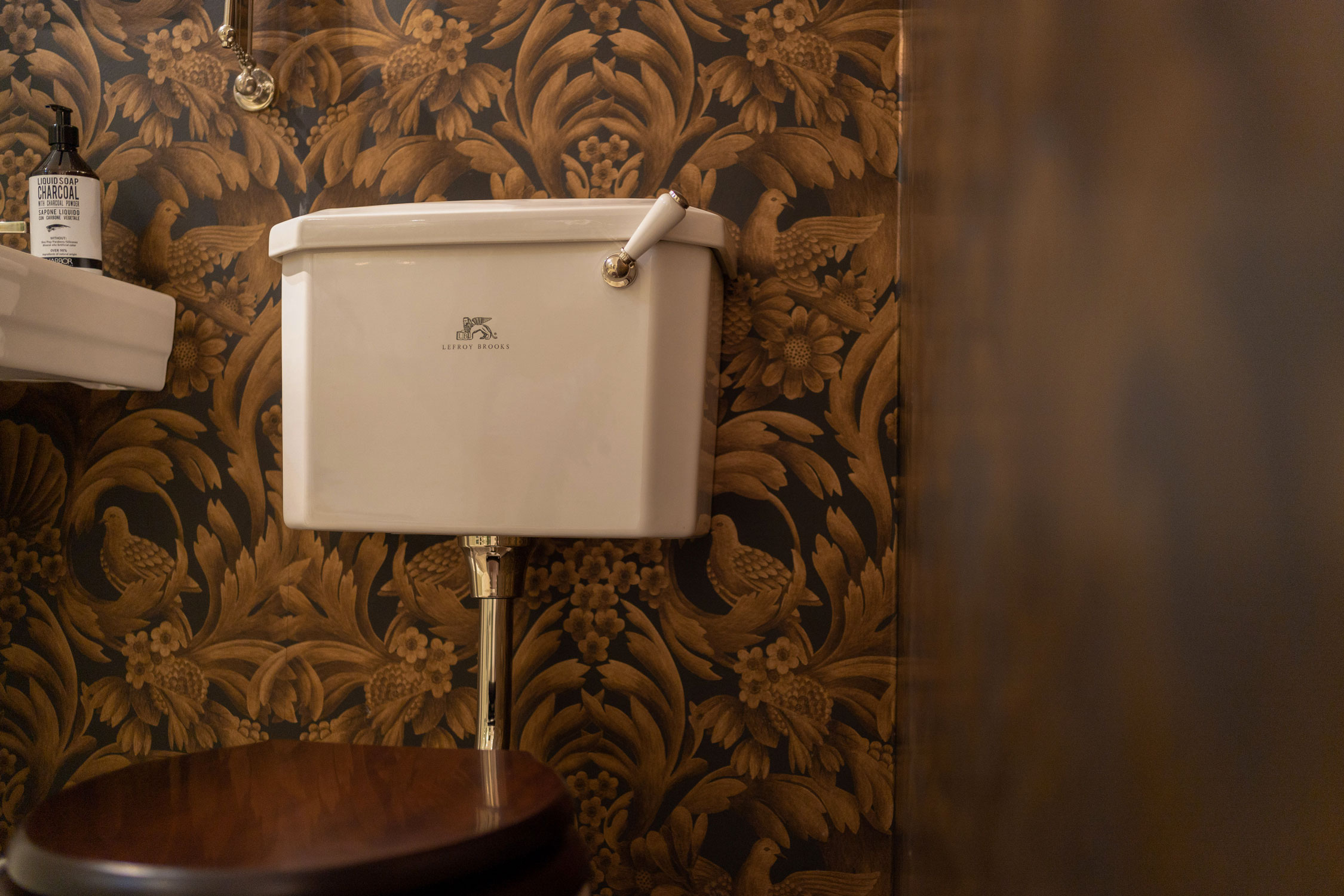 Close up of lefroy brooks toilet with dark brown wallpaper.