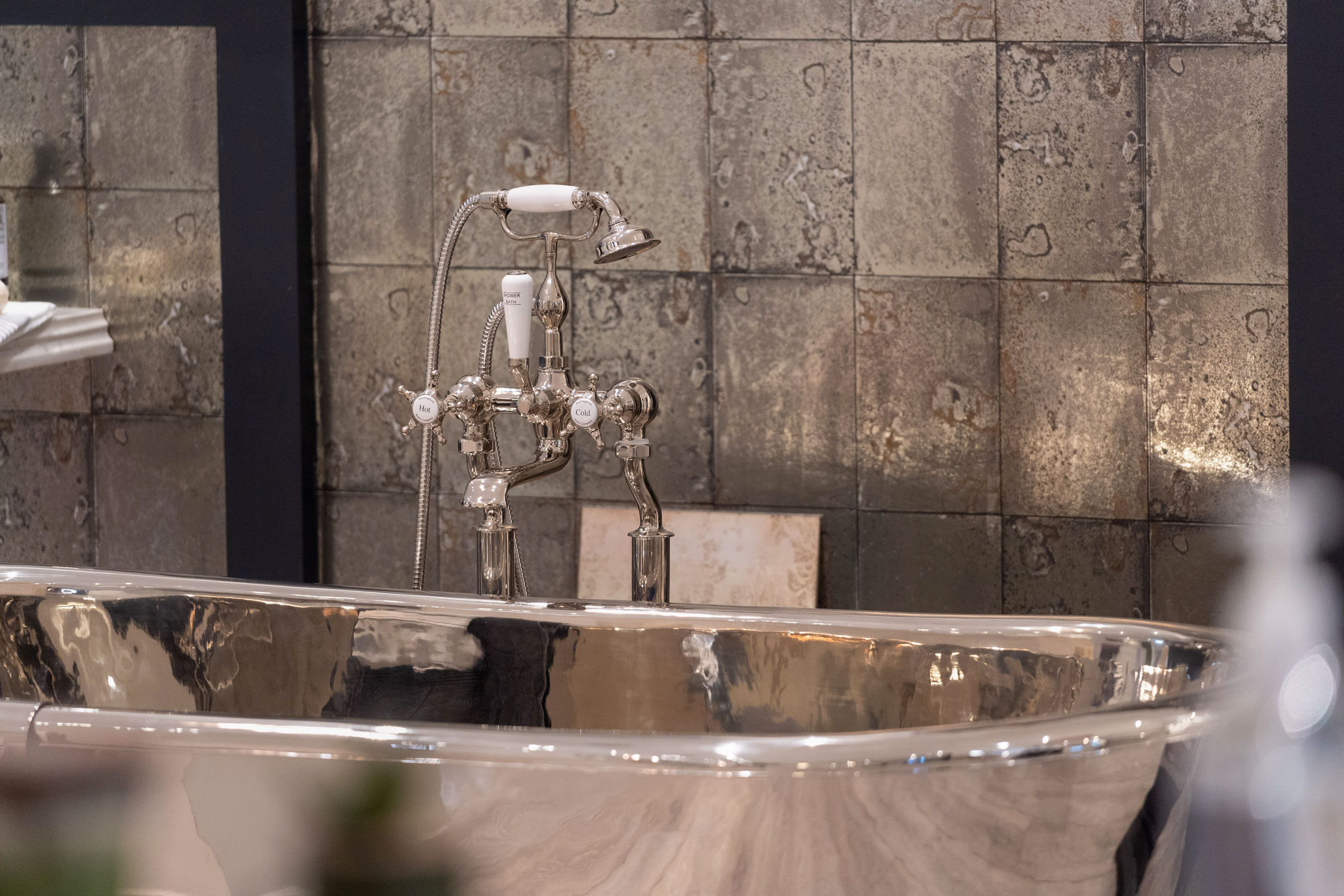 Artisitc photo of large chrome bath with large shiny tiles in background.